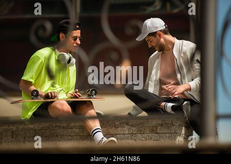 Two male friends are sitting on the wall and talking about the skate Stock Photo