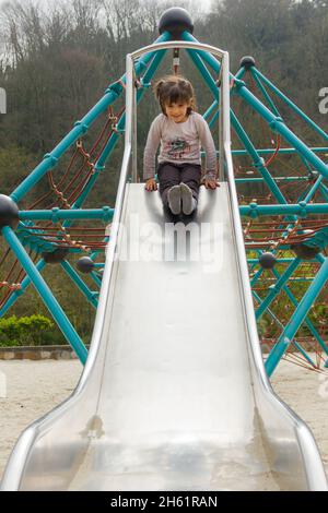 Smiling little girl ready to go down on sliding board at park on cloudy day in Bilbao. Sequence one of three Stock Photo
