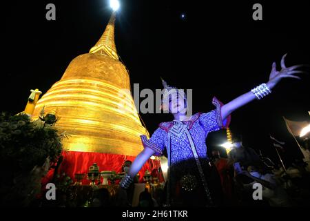 Bangkok, Thailand. 12th Nov, 2021. A dancer performs in front of Wat Saket Temple, also know as Golden Mountain during the temple and wrapped red cloth around the golden Mountain. Devotees assembled to wrap sacred red cloth around the Golden Mount chedi, signifying the start of Wat Saket festival. Before the faithful lined up for a multicultural parade consisting of lion dancers, traditional Thai dancers, students from the temples school and spiritual brahmans. Names of families and loved ones were written onto the long stretch more than hundred meters of fabric in hopes of securing good fortu Stock Photo