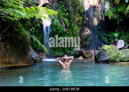 woman in a swimsuit on the background of a waterfall in the lagoon, woman bathing in the thermal pools of Caldeira Velha, Sao Miguel, Azores, Portugal Stock Photo