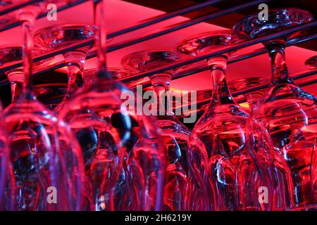 Wine glasses hanging down from red light rack inside bar. Night club, party disco concepts Stock Photo