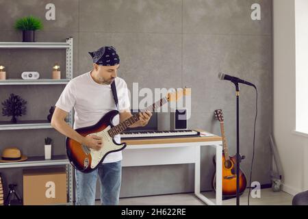 Focused and enthusiastic adult rocker man playing electric guitar in home studio. Stock Photo