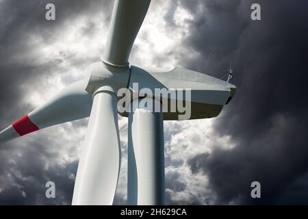 Red and white wind turbine against a gray sky with storm clouds and copy space. Renewable energy concept. Stock Photo