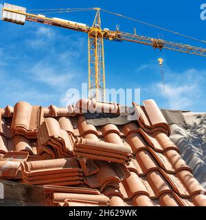 Orange crane and a closeup of a roof under repair with terracotta orange tiles (Pantiles, Coppo in Italian language). Construction industry concept. Stock Photo