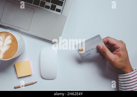Top view man holding a credit card and on the desk. Laptop computer Notepad and pen.Online shopping business, pay by credit card Stock Photo