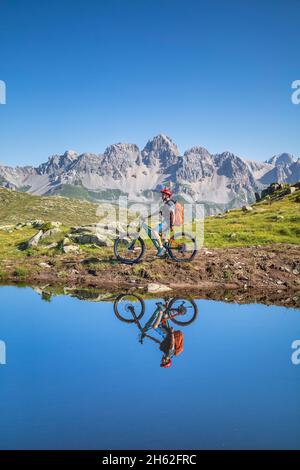 man,22 years old,cyclist with e-bike near an alpine lake,cyclist reflected in the water of a mountain lake,mountains in the background. laresei,falcade,belluno,veneto,italy