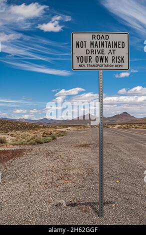 Tonopah, Nevada, US - May 16, 2011: Closeup of road sign warning road is not maintained, drive at your own risk against blue cloudscape. Gray mountain Stock Photo