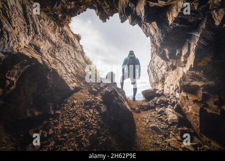 lonely man,35 - 40 years old,hiker in the backlight at the entrance to a cave in the mountains,col di lana,dolomites,livinallongo del col di lana,belluno,veneto,italy Stock Photo