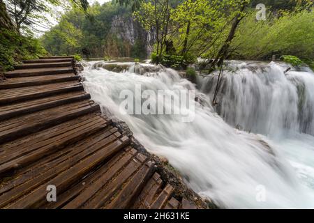 a wooden walkway surrounded by trees,waterfalls and greenery in plitvice national park,croatia Stock Photo