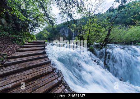 a wooden walkway surrounded by trees,waterfalls and greenery in plitvice national park,croatia Stock Photo