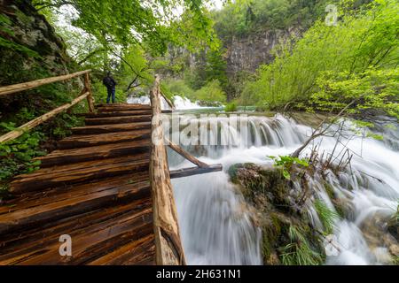 a wooden walkway surrounded by trees,waterfalls and greenery in plitvice national park,croatia Stock Photo