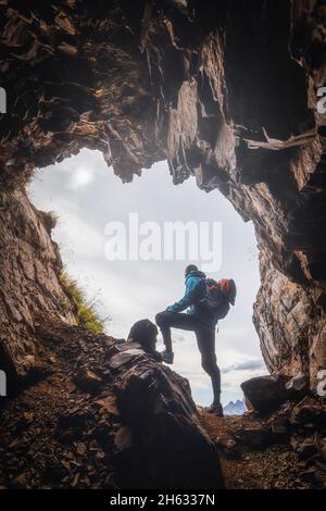lonely man,30-35 years old,hiker in the backlight at the entrance to a cave in the mountains,col di lana,dolomites,livinallongo del col di lana,belluno,veneto,italy Stock Photo