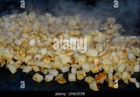 Hash browns being cooked on a griddle, with steam rising from the small cubed potatoes