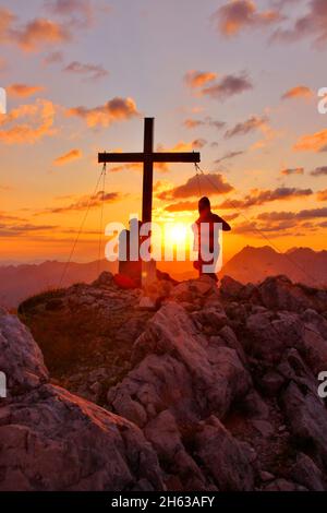 two young women on a hike,obere wettersteinspitze,2.297m,summit cross,sun,sun ball,germany,bavaria,upper bavaria,werdenfelser land,mittenwald,isar valley Stock Photo