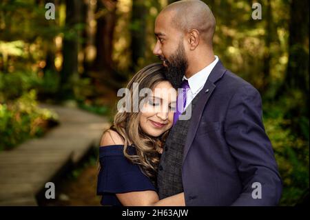 Full of love photo of an affectionate mixed race young couple holding each other in the woods in the Lynn Canyon Park, North Vancouver, British Columb Stock Photo