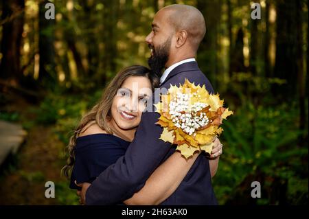 Full of love photo of an affectionate mixed race young couple holding each other in the woods in the Lynn Canyon Park, North Vancouver, British Columb Stock Photo