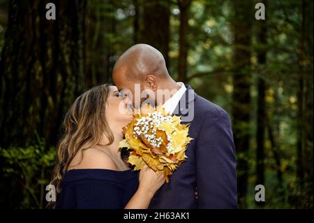 Full of love photo of an affectionate mixed race young couple kissing in the woods in the woods in the Lynn Canyon Park, North Vancouver, British Colu Stock Photo