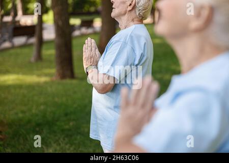 Concentrated mature man meditates doing yoga with woman in park Stock Photo