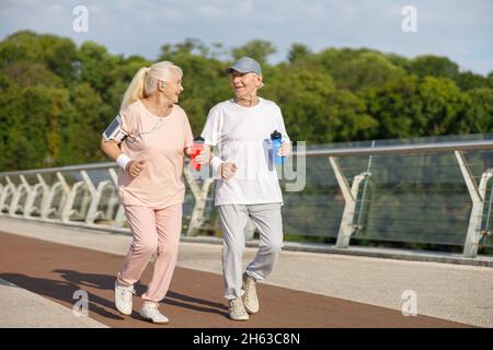 Happy senior couple with bottles runs training together on footbridge Stock Photo