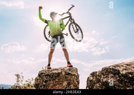 Latin thrilled male cyclist carrying his bike above his head after finishing riding on mountain Stock Photo