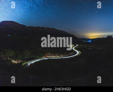 light trail of cars on a winding road with the stars above (milkey way ...