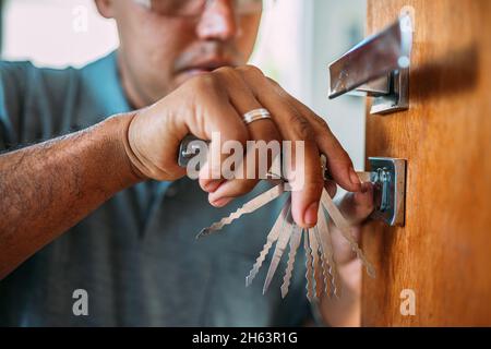Locksmith opening a door. Close-up of male hands repair or installing a metal door lock with a screwdriver. Improved robbery protection. Lockpicker. Stock Photo