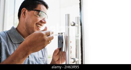 Close-up of male hands repair or installing a metal door lock on glass door. Stock Photo