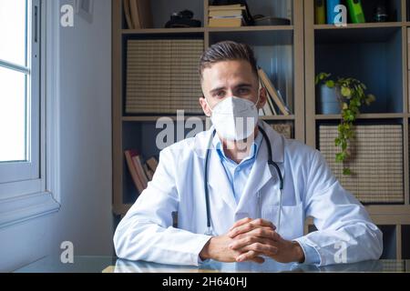 portrait of confident professional male doctor wearing medical protective face mask and uniform with stethoscope standing in hospital office with arms crossed,looking at camera,healthcare concept Stock Photo
