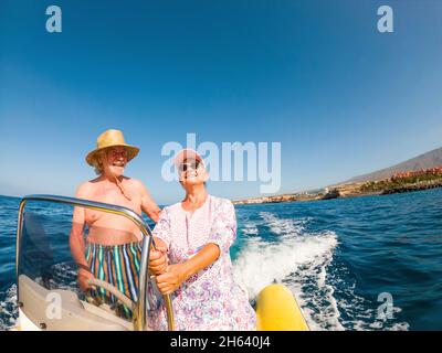 beautiful and cute couple of seniors or old people in the middle of the sea driving and discovering new places with small boat. mature woman holding a phone and taking a selfie with hew husband Stock Photo