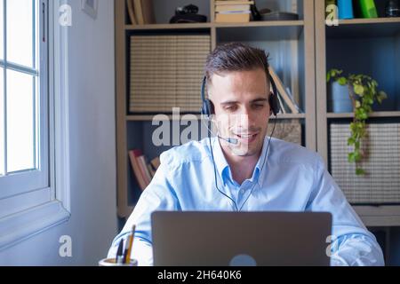 attractive caucasian man sit at homeoffice room wearing headset take part in educational webinar using laptop. video call event with clients or personal chat with friend remotely concept Stock Photo