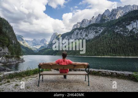 man relaxing on bench in front of dachstein mountains reflected in gosau lake,austria. Stock Photo