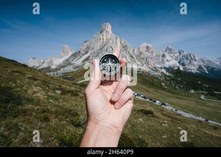 hand holding compass against passo giau mountains in background in dolomites alps,italy. travel adventure concept. Stock Photo