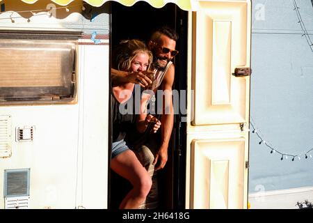 young alternative millennial couple laugh a lot standing inside old caravan tiny house - travel and disconneted lifestyle young people enjoying out of the box and off grid life Stock Photo
