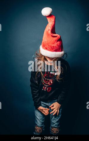 studio shot of a child wearing a christmas hat and pullover making fun in front of a blue background Stock Photo