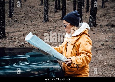 portrait of woman enjoy travel in the nature forest woods with car - female people look the map on the nose of the vehicle lost in adventure trip - adult beautiful lady in alternative outdoor leisure lifestyle Stock Photo