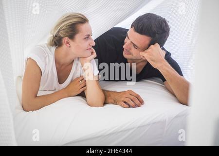 young couple lying on front and staring at each other. beautiful couple spending leisure with each other. loving couple looking at each other on cozy bed at home Stock Photo