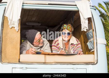 happy senior retired couple in retro vintage style van or camper planning a trip looking at map. old couple enjoying holiday traveling in camper. cheerful elderly couple on summer vacation Stock Photo