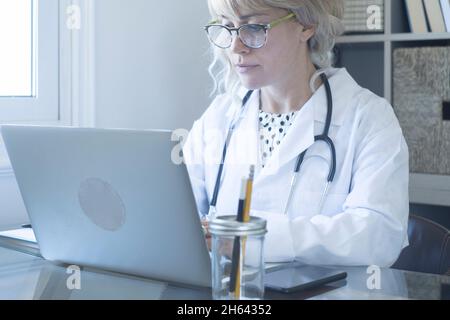 female doctor working on laptop for consultation. caucasian woman using computer on desk in home office. female frontline worker attending video calls for consultation from patients using her laptop Stock Photo