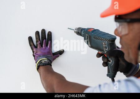 Confident Latin male holding drill on wall. Stock Photo