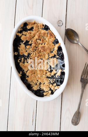 Blueberry crumble pie in oval white cooking pan with old silverware overhead view Stock Photo
