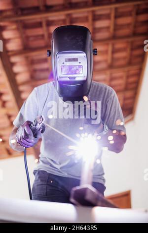 Close up portrait view of protected professional mask welder man working on metal sculpture in a house under construction.