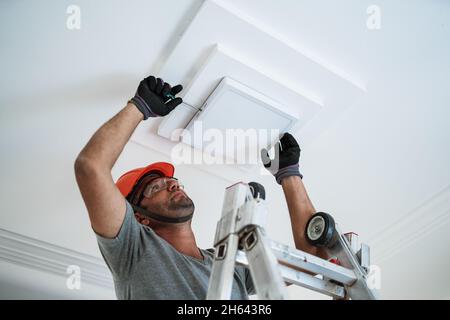 Latino electrician installing a led light on the ceiling. Stock Photo