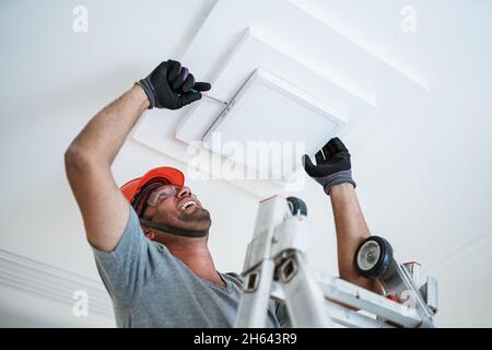 Latino electrician installing a led light on the ceiling. Stock Photo