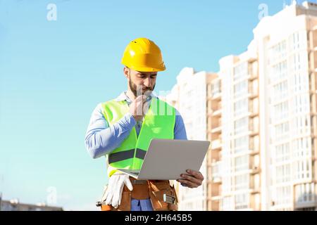 Thoughtful construction worker using laptop outdoors Stock Photo