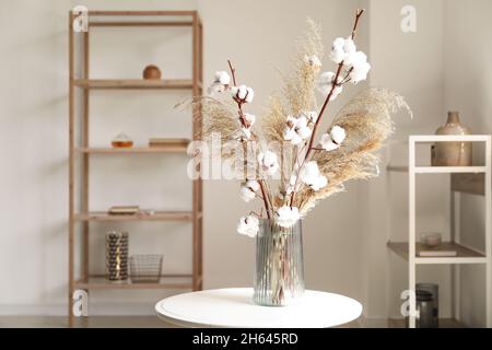 Vase with pampas grass and cotton branches on table in room Stock Photo