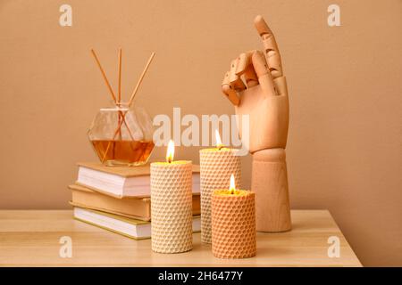 Burning candles, wooden hand, stack of books and reed diffuser on wooden table near color wall Stock Photo