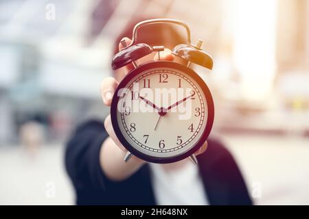 closeup business people hand holding alarm bell clock outdoor blur office city background Stock Photo
