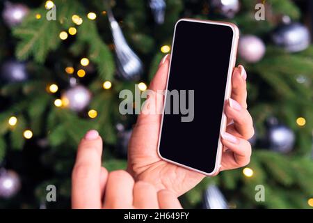 Hand holding blank screen smartphone on bokeh from christmas tree light can use for design, christmas concept. empty space for design Stock Photo