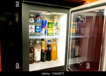 Water and soda soft drink bottles, energy drinks, coke, red bull in small typical fridge of minibar with an open door in a hotel