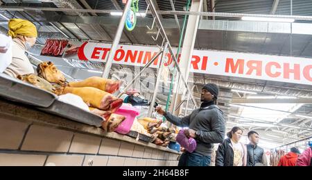 A young Black man buying meat from the counter with sheep heads and legs in meat market in Altyn Orda, Almaty, Kazakhstan Stock Photo